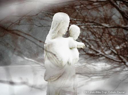 This is a picturesque winter scene of a snow covered statue of the Blessed Virgin Mary holding the Child Jesus.